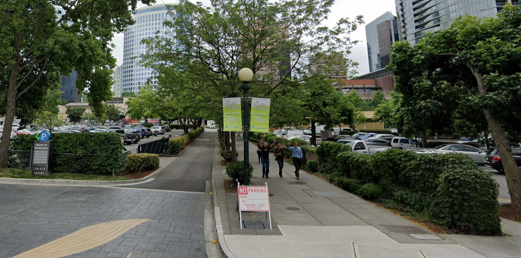 A photo of a sidewalk and narrow street running between two surface level parking lots.