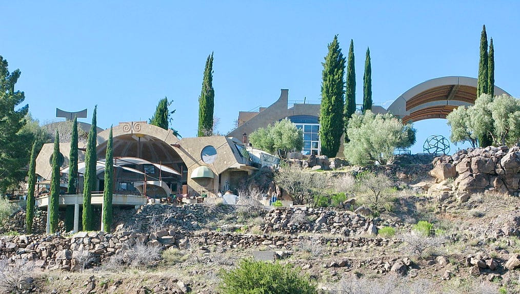 A photo of the some brown curved buildings in the desert with a few trees and shrubs nearby. 