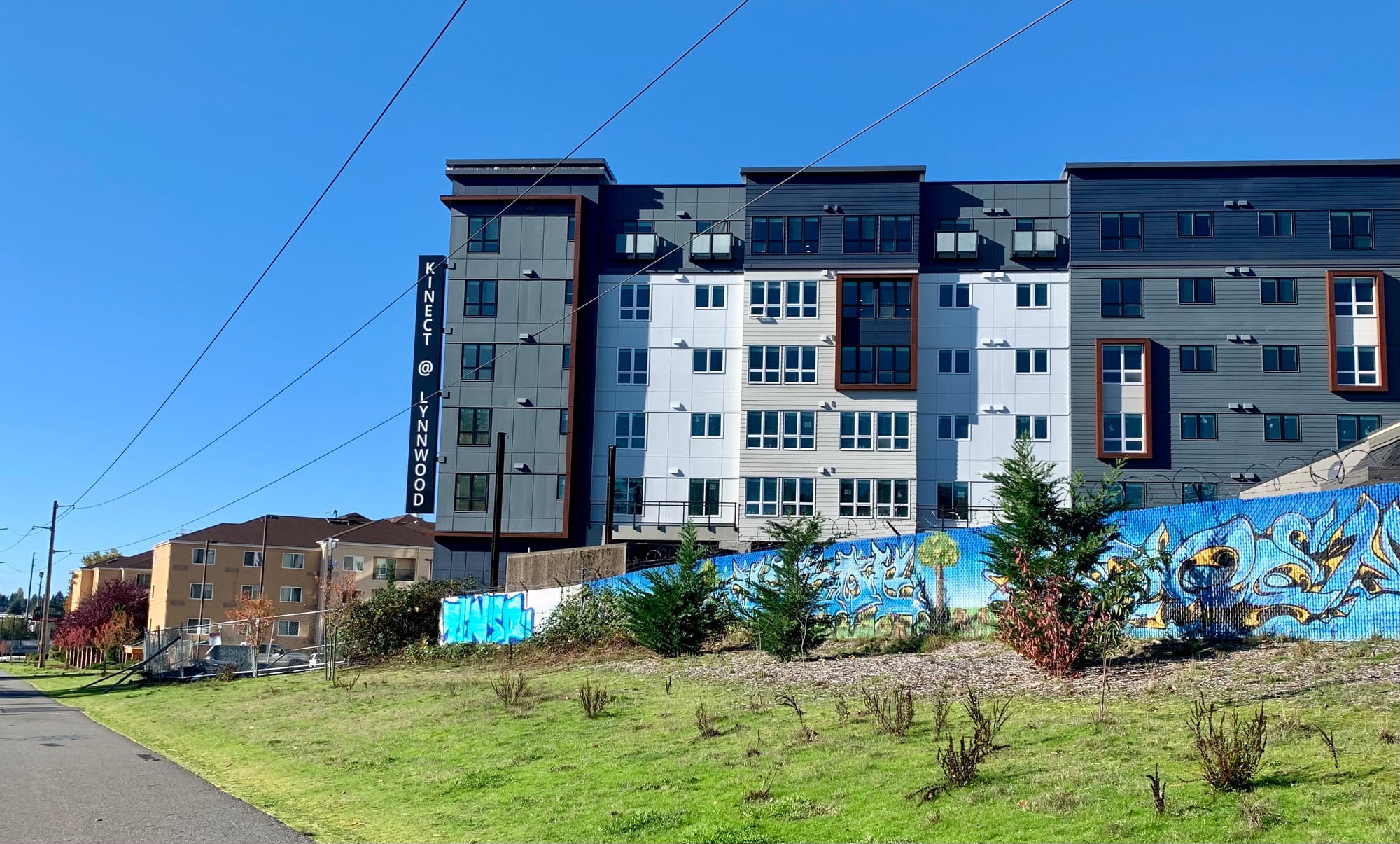A photo of a six story apartment building next to a multi-use trail.