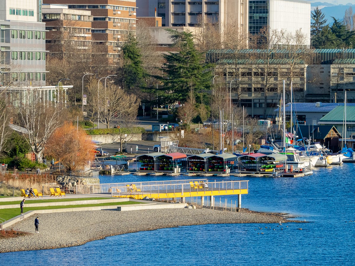 A photo of a pier with chairs over looking a lake with boats in the background. 