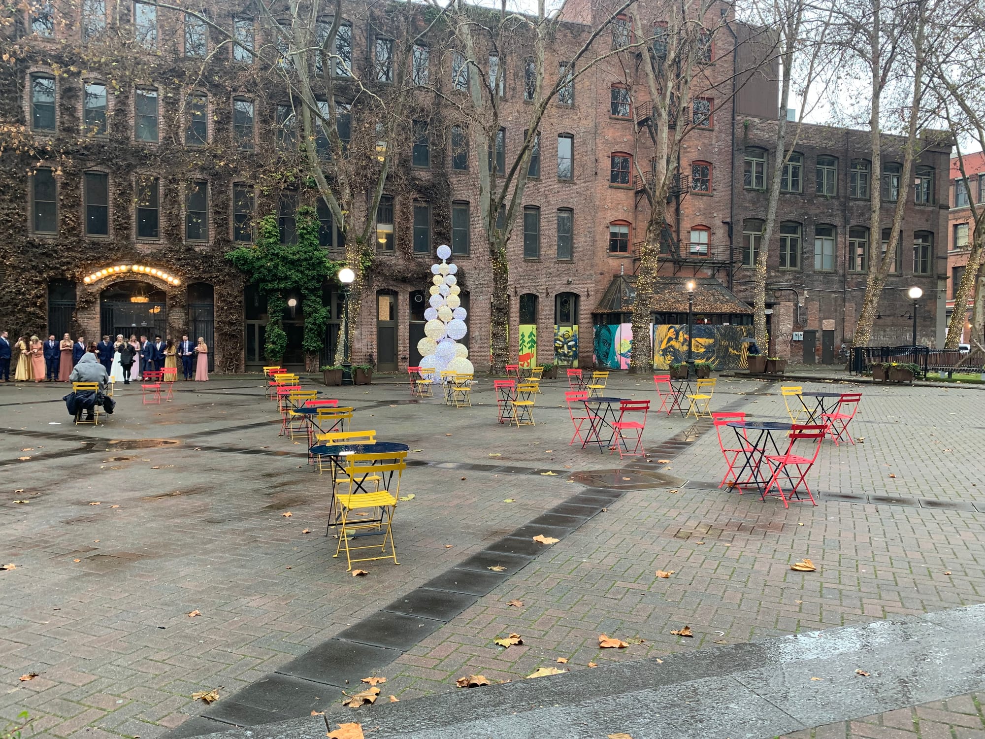 A plaza with Christmas lights and many empty tables.