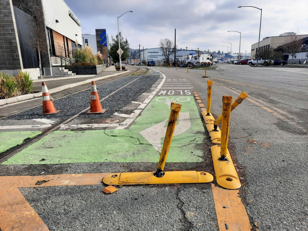 Orange cones and flex posts mark the path with gravel beyond. One flexpost is crooked, likely from being run over by a motor vehicle.