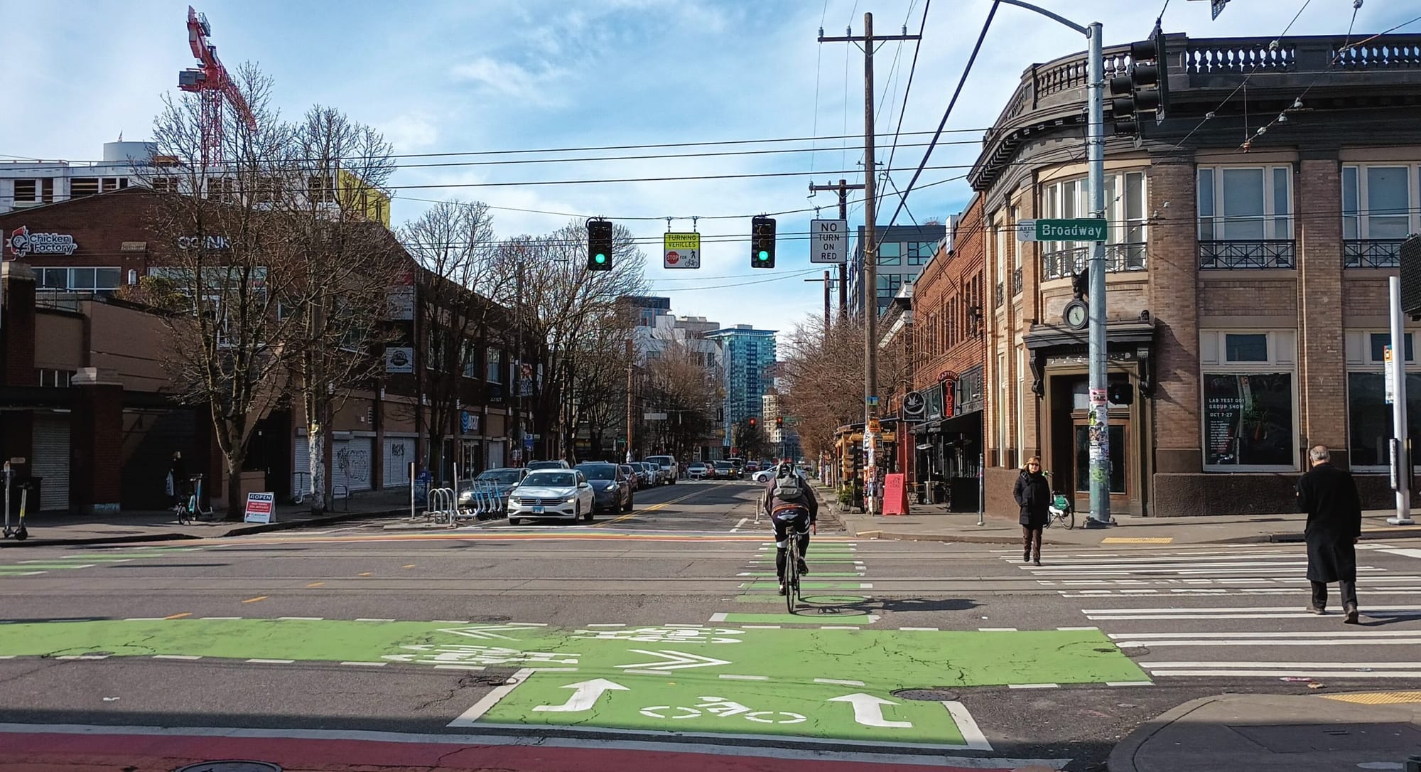 
                     Someone on a bike crosses the street as pedestrians walk in a crosswalk and drivers wait to turn at Broadway and Pike in Seat
                     