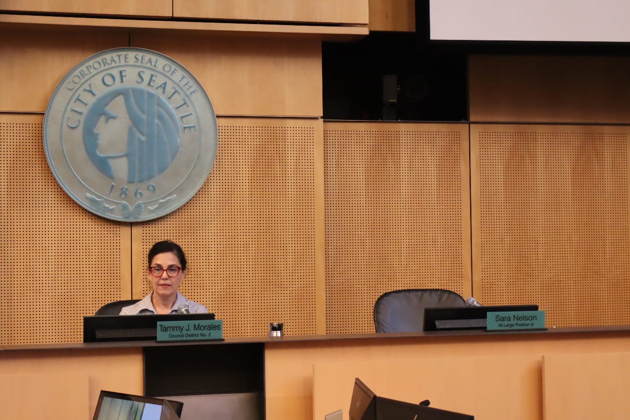 Morales sits at the dais with the city seal above.