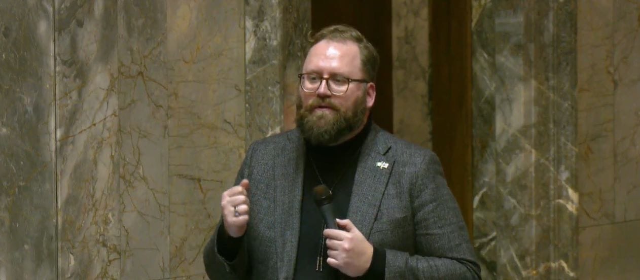 Marko is a White man with a big brown beard and glasses. He wears a grey suit coat with no tie.