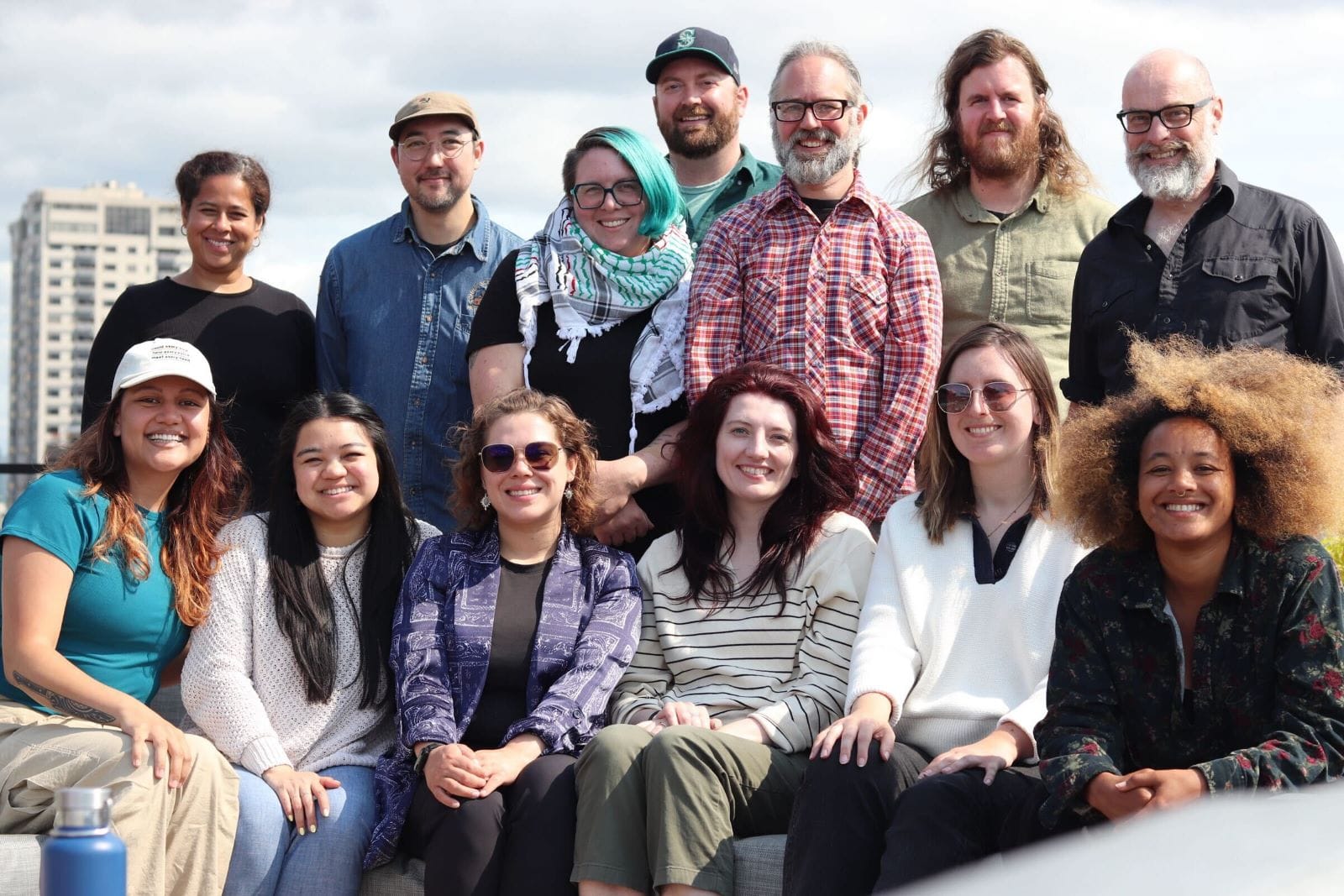 The group stands on a rooftop with the Seattle skyline and Elliott Bay in the background.