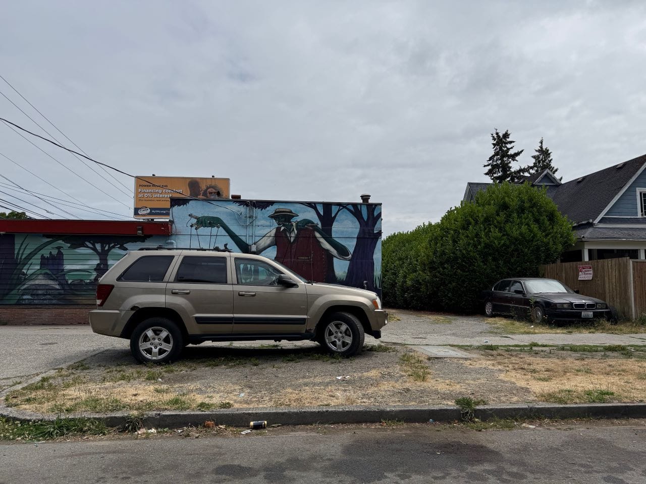 A SUV parks on a strip of dry brown grass along a street with a billboard in the background.