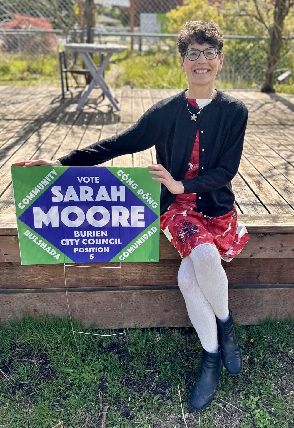 Moore sits on a wooden deck posing with her campaign sign