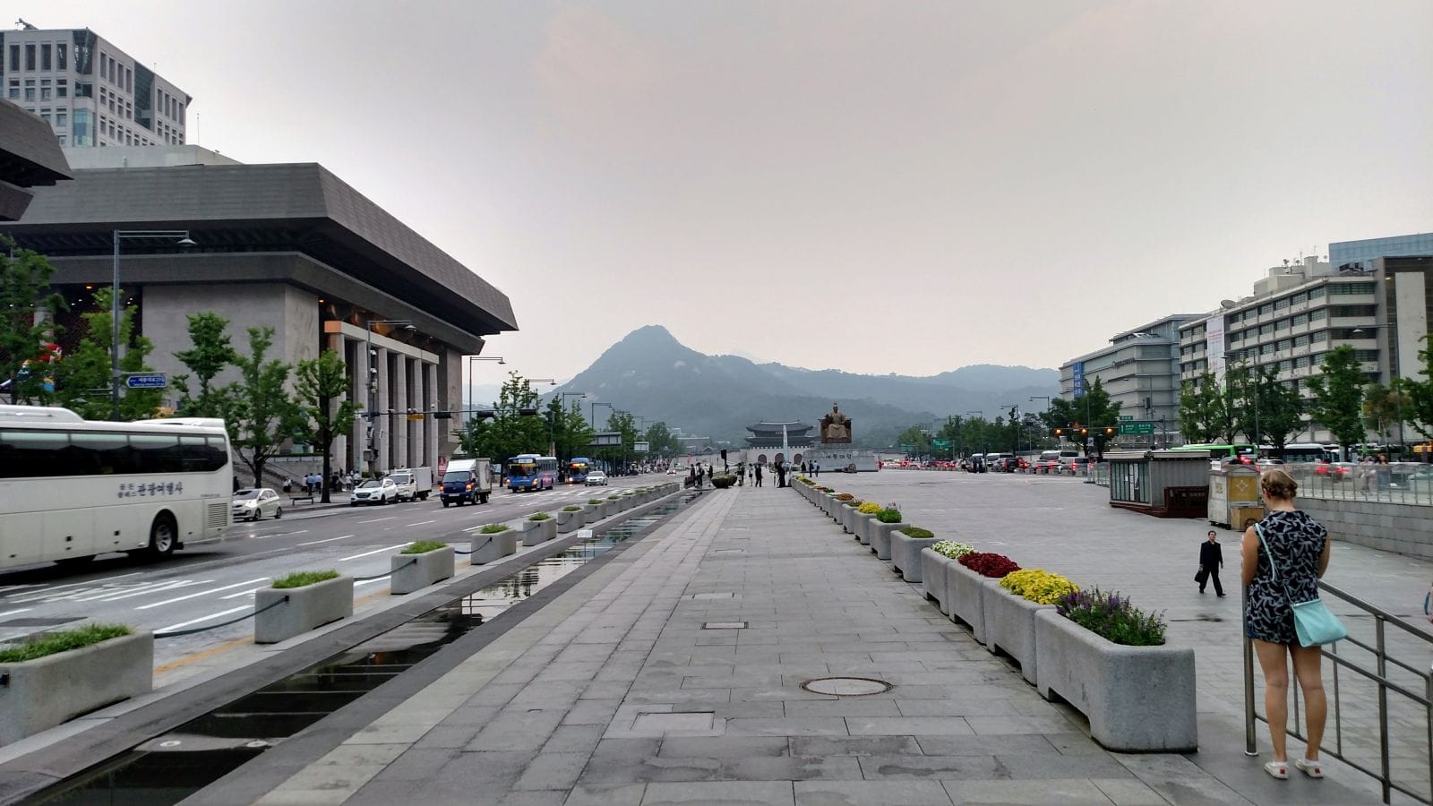 A busy road borders both sides of the wide linear park with a mountain in the distance.