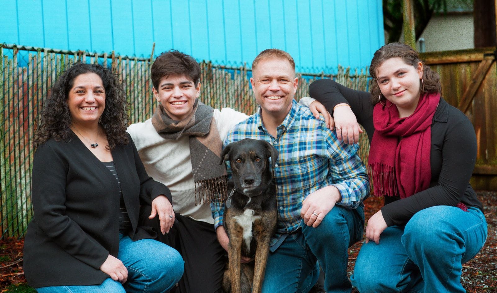 The Jenks family crouches and her husband holds the family dog. Her two teenage kids wear scarves.